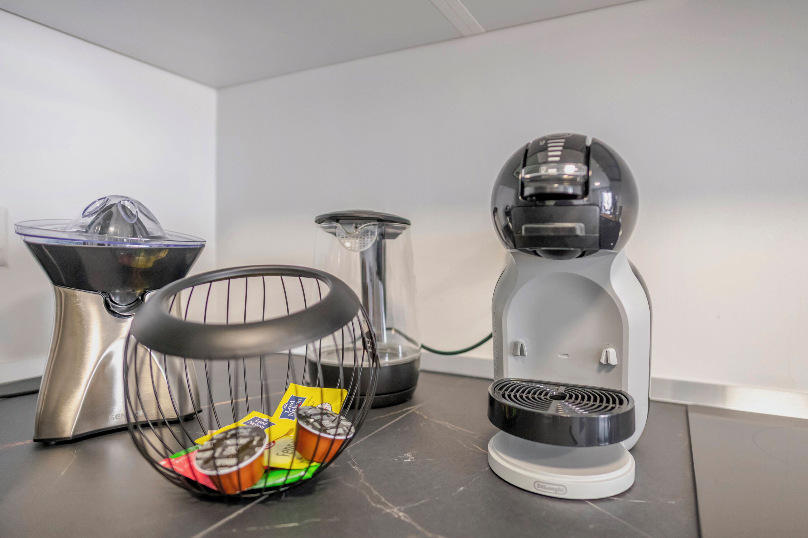 A kitchen with a juicer, blender, and a basket containing food items.
