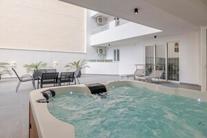 A rooftop pool area with lounge chairs, a hot tub, and a glass-enclosed balcony.