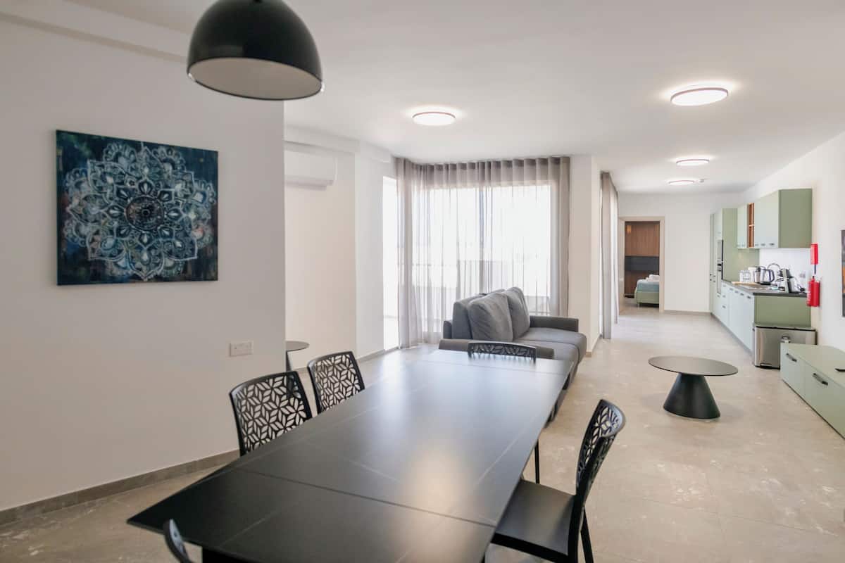 Une cuisine moderne avec des meubles de couleur verte, un coin repas avec une longue table et des chaises, et un salon avec un canapé et des rideaux.