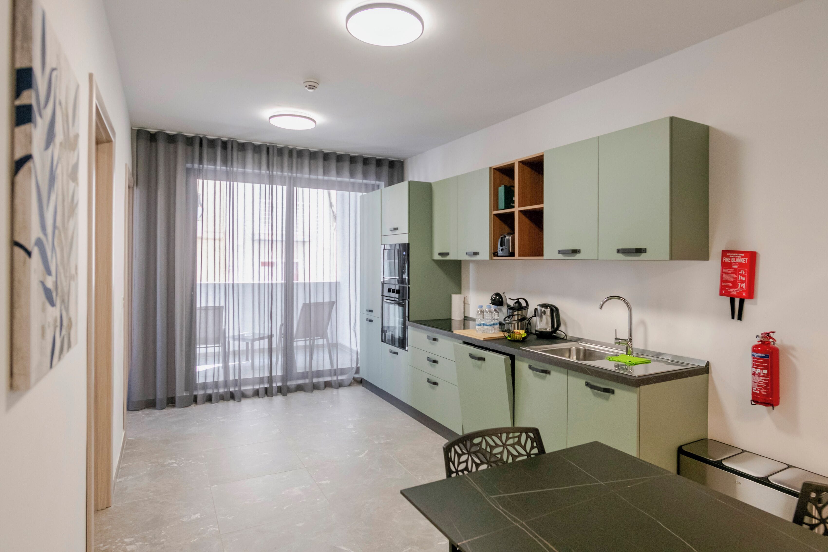 Une cuisine compacte avec des meubles de couleur verte, un évier et un coin repas comprenant une table et des chaises.