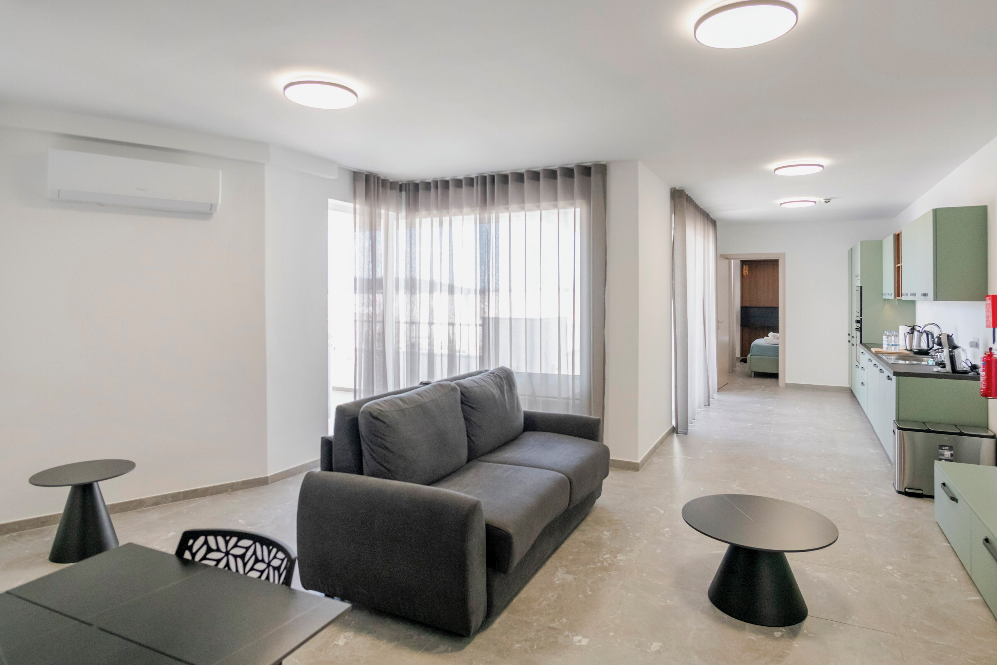 A modern living room with a sofa, two tables, and a kitchen area with cabinets and a sink.