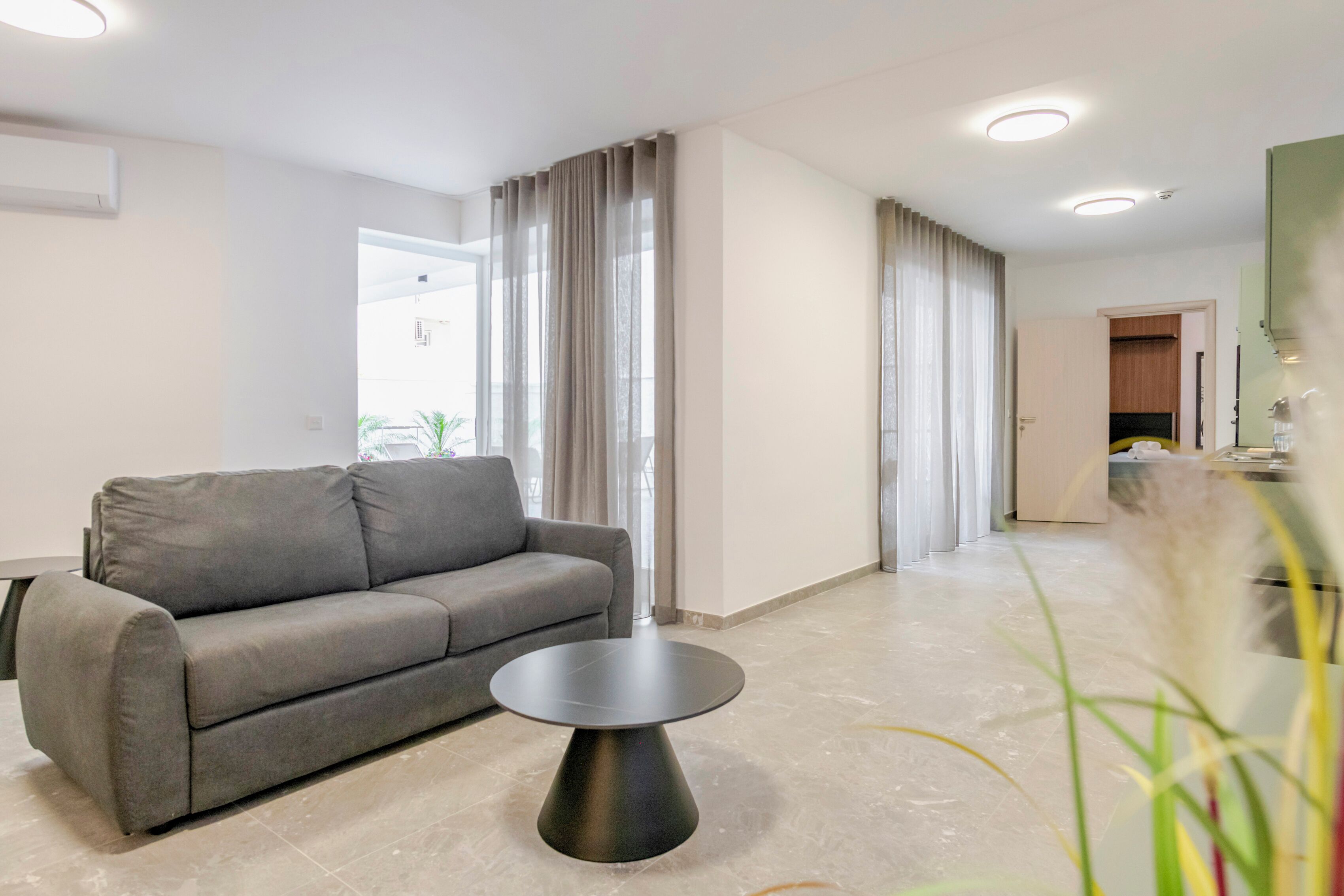A modern living room with a grey sofa, a round black coffee table, and a kitchen area in the background.