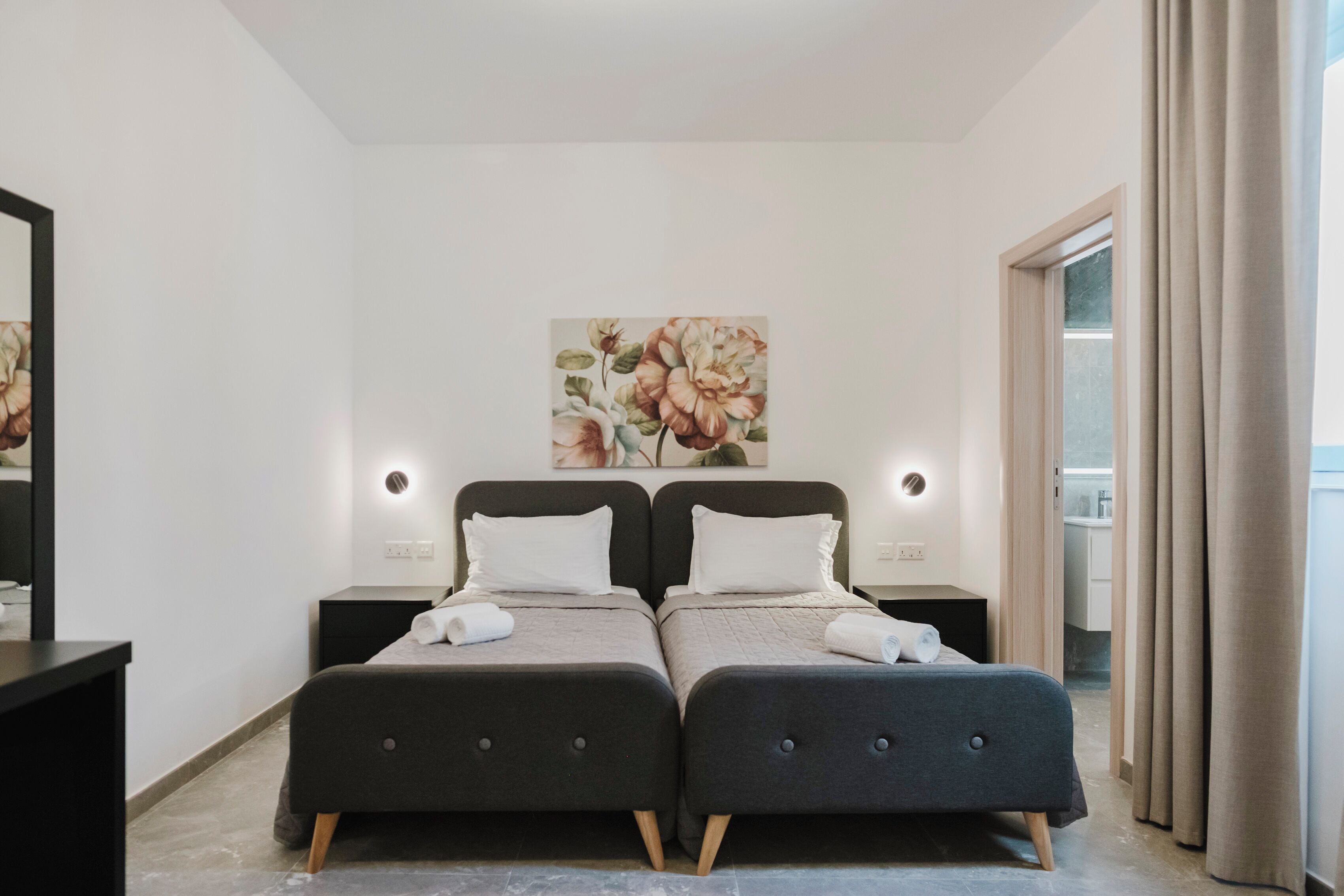 Et moderne hotelværelse med to senge, et stort blomsterkunstværk på væggen og udsigt over byen gennem vinduet.