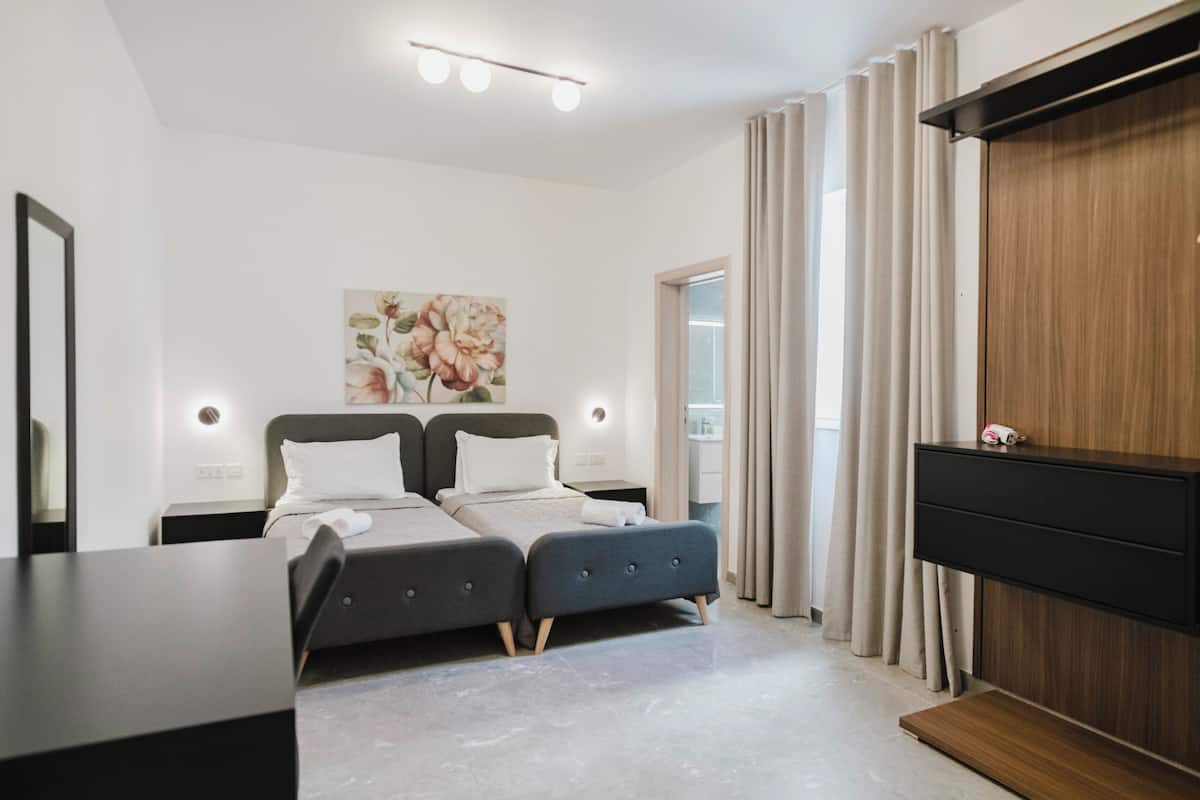 Une chambre moderne avec deux lits, une armoire en bois, un téléviseur à écran plat et une grande fenêtre avec des rideaux.