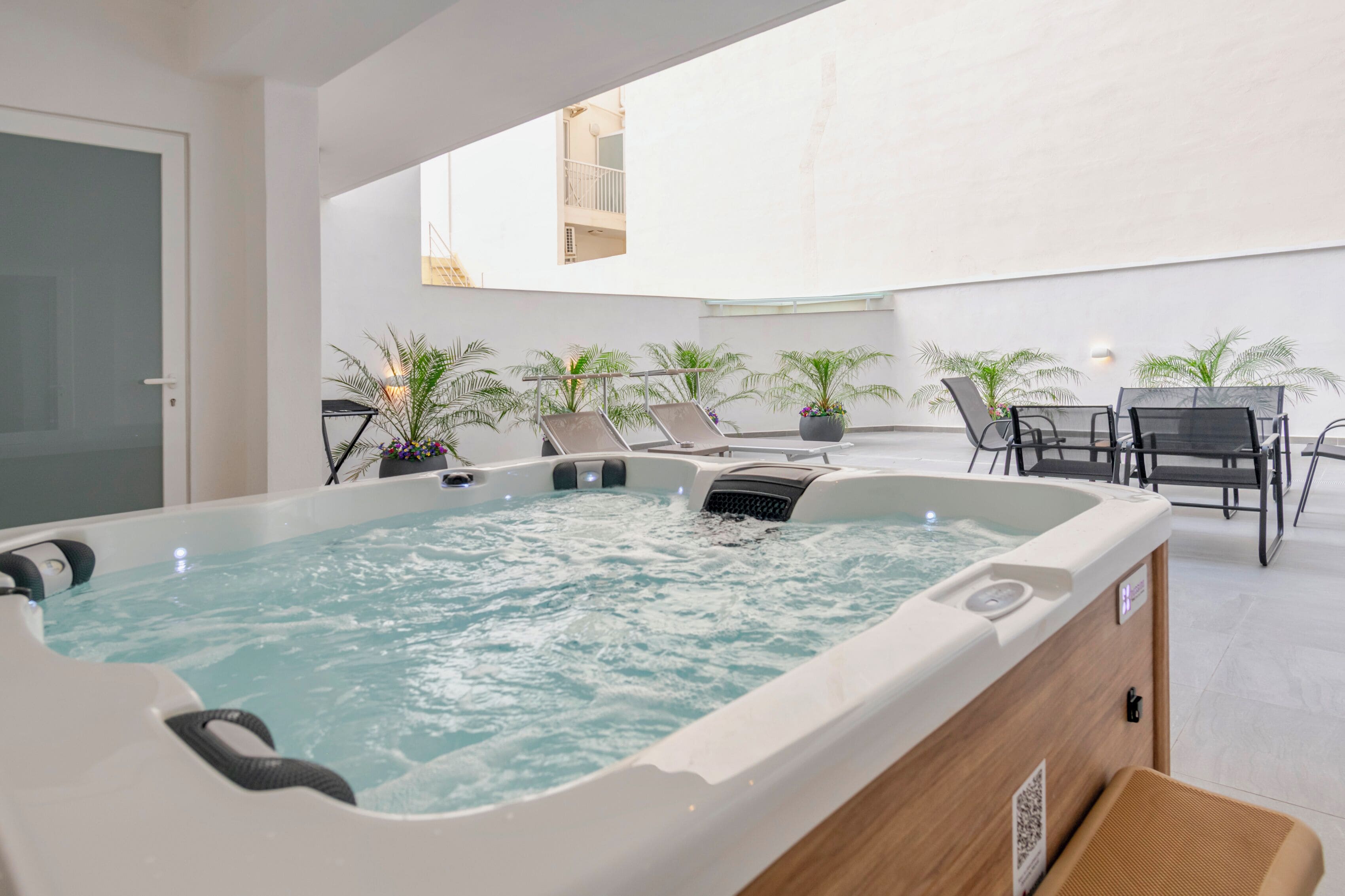 Een bubbelbad in een ruim buitengebied met een tafel en stoelen, omgeven door potplanten.