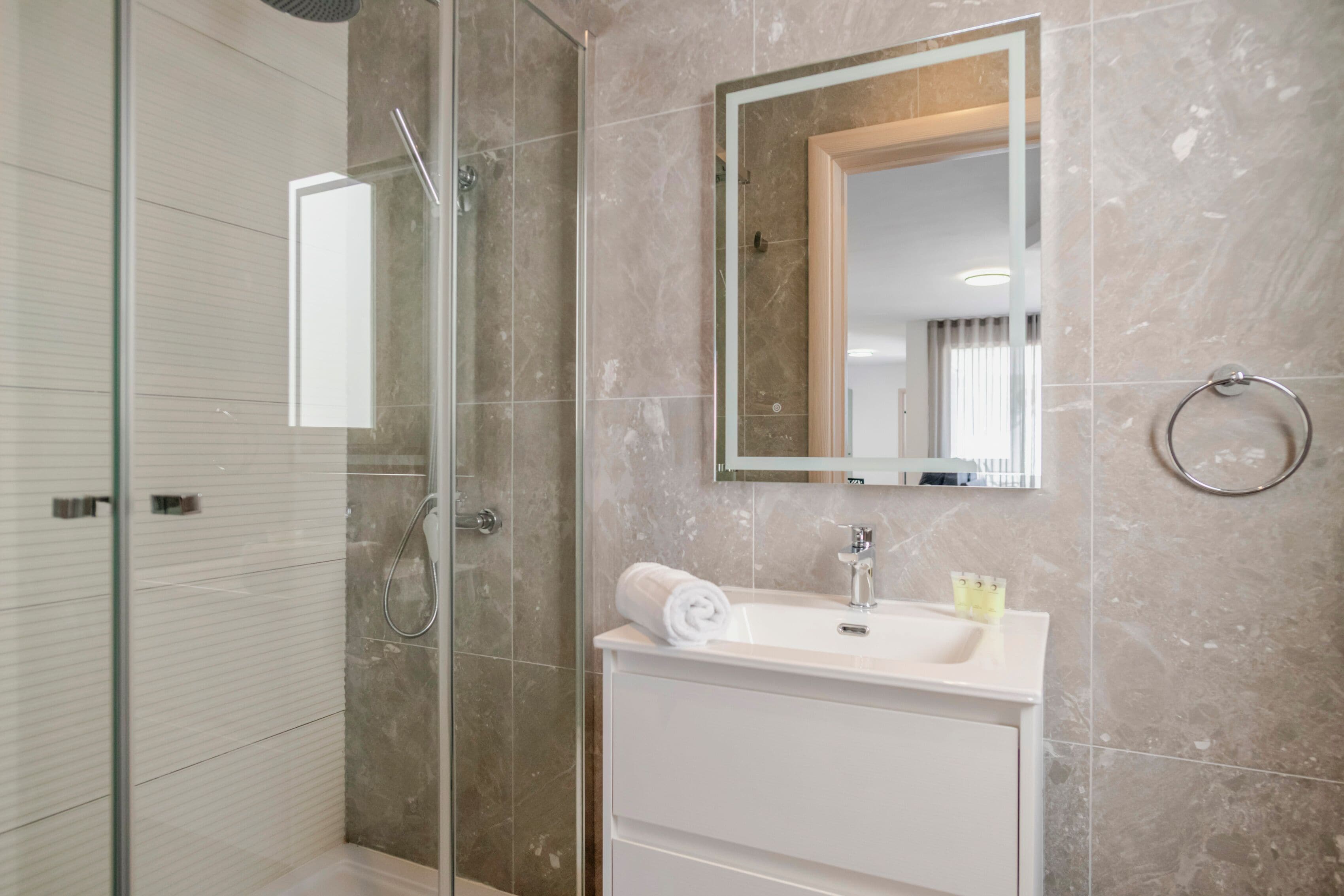 A modern bathroom with a glass shower enclosure, a white sink with a mirror above it, and a towel on the sink.