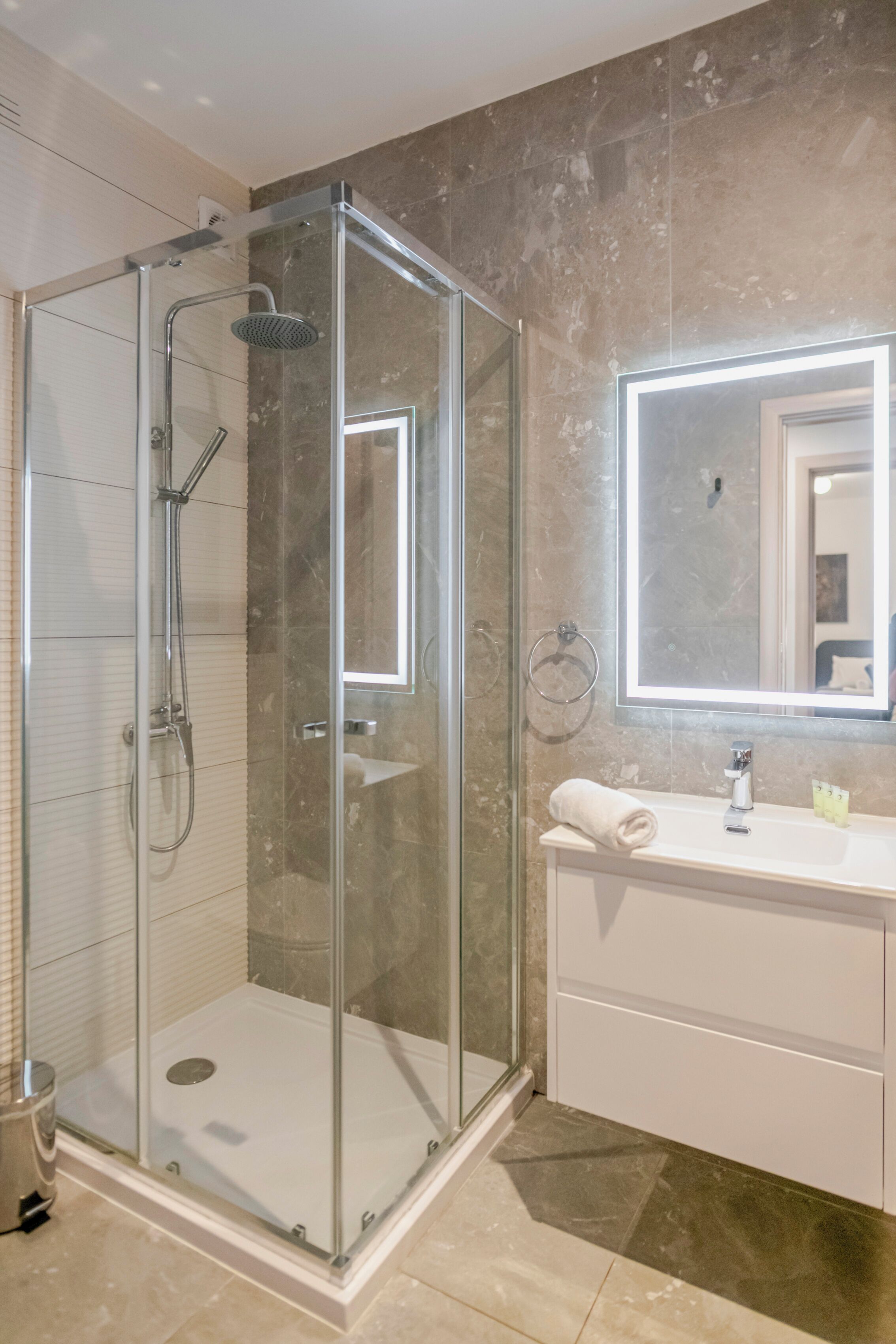 A modern bathroom with a glass-enclosed shower, a vanity with a mirror, and a towel rack.