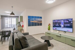A modern living room with a flat-screen TV, grey sofa, dining table, and a cityscape painting.