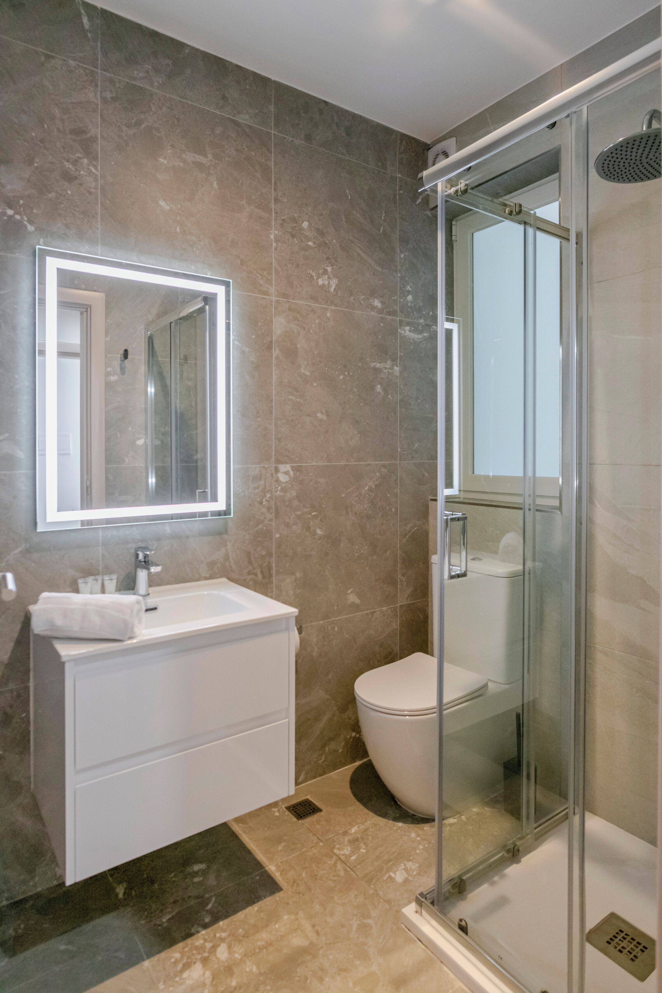 Ein modernes Badezimmer mit einer gläsernen Dusche, einem weißen Waschbecken und einem großen Spiegel.
