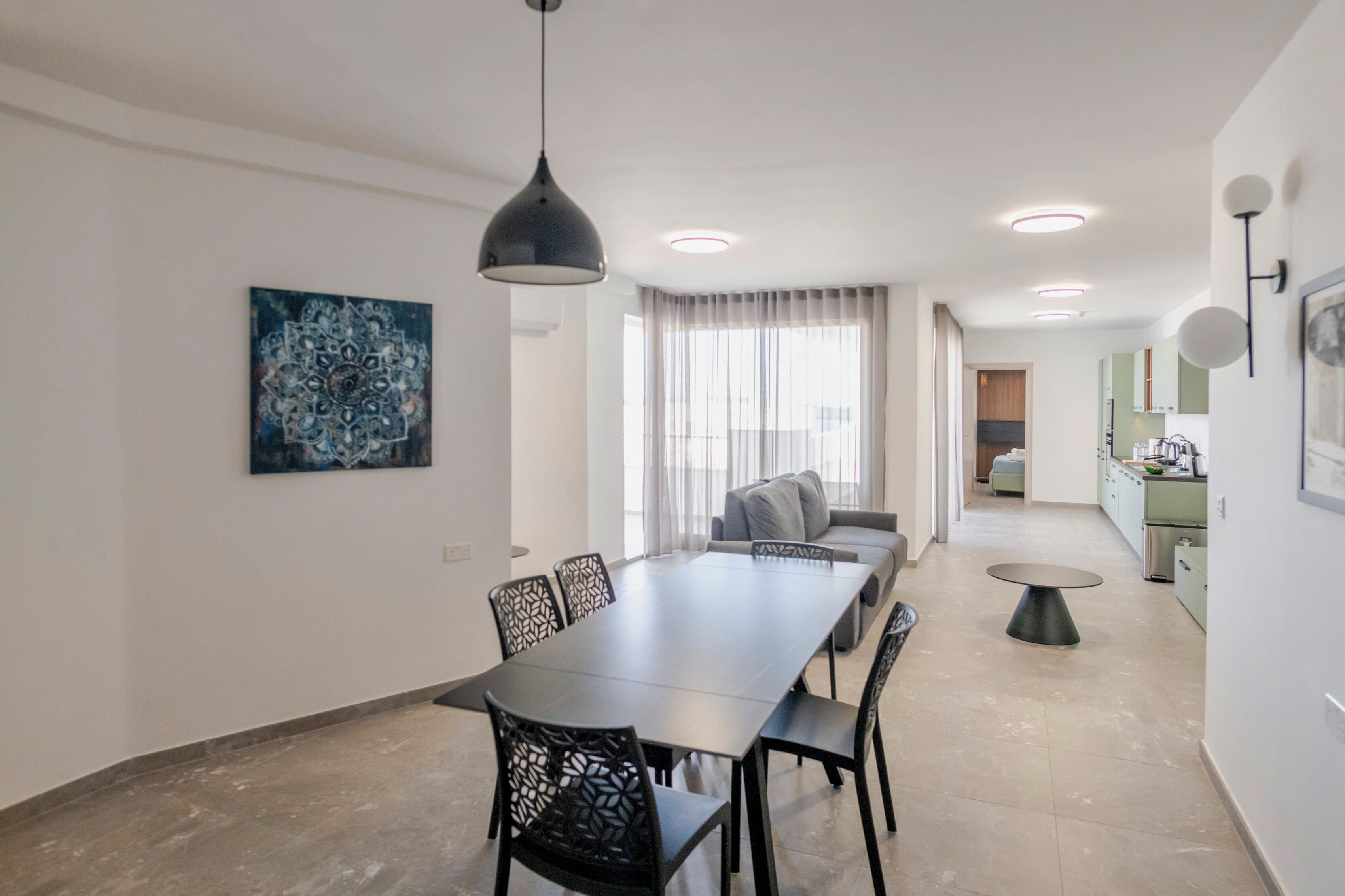 Un espace de repas moderne avec une longue table et des chaises, un canapé et une cuisine en arrière-plan.