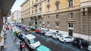 A street view with parked cars, a building with classical architecture, and a sign indicating a public space.