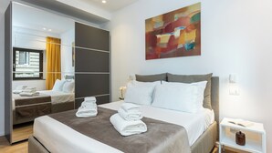 A modern hotel room with a large bed, a bedside table with a lamp, a mirror, and a colorful abstract painting on the wall.