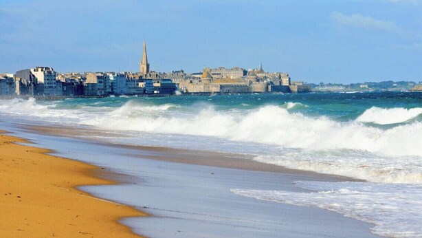 A coastal cityscape with a prominent church spire, a fortified structure, and a sandy beach. - Charming apartment just steps from the beach (Saint-Malo)