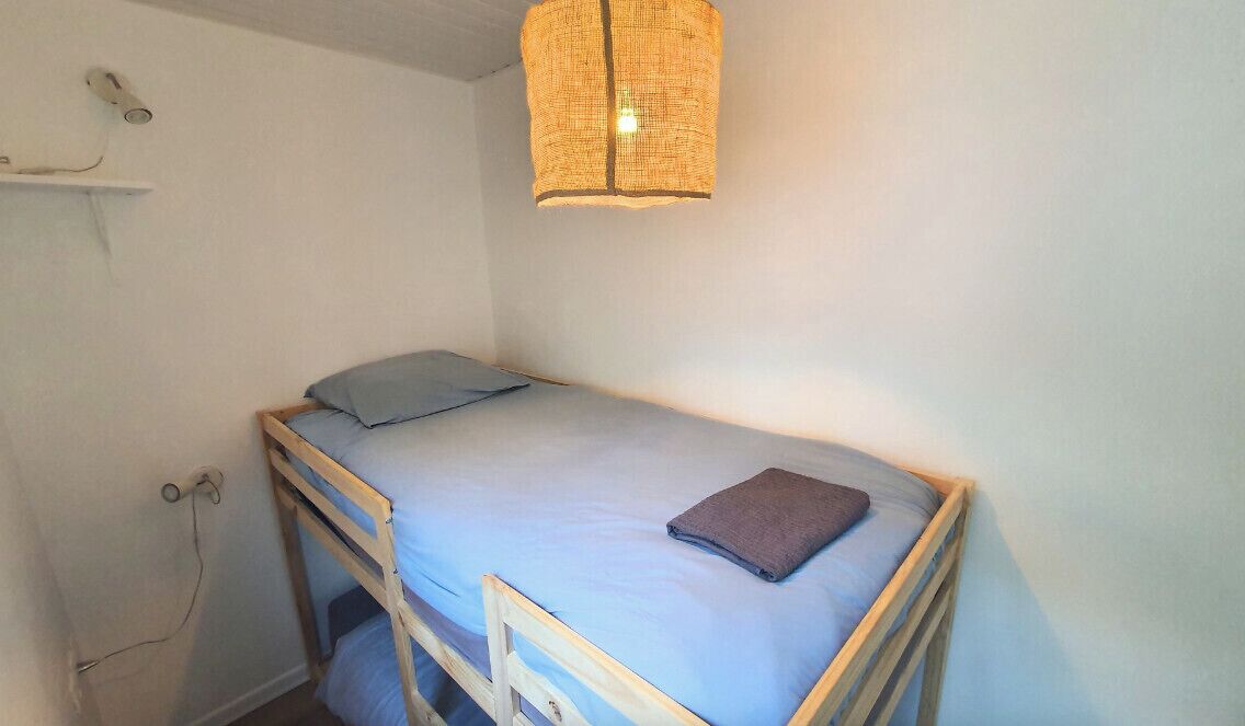 Una cama litera con un colchón azul y una almohada, un estante pequeño con un secador de pelo, y una lámpara de fibra sobre la cama.