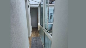 A narrow hallway with a wooden floor and a gray rug, leading to a room with a large window and a white door. - Charming apartment just steps from the beach (Saint-Malo)