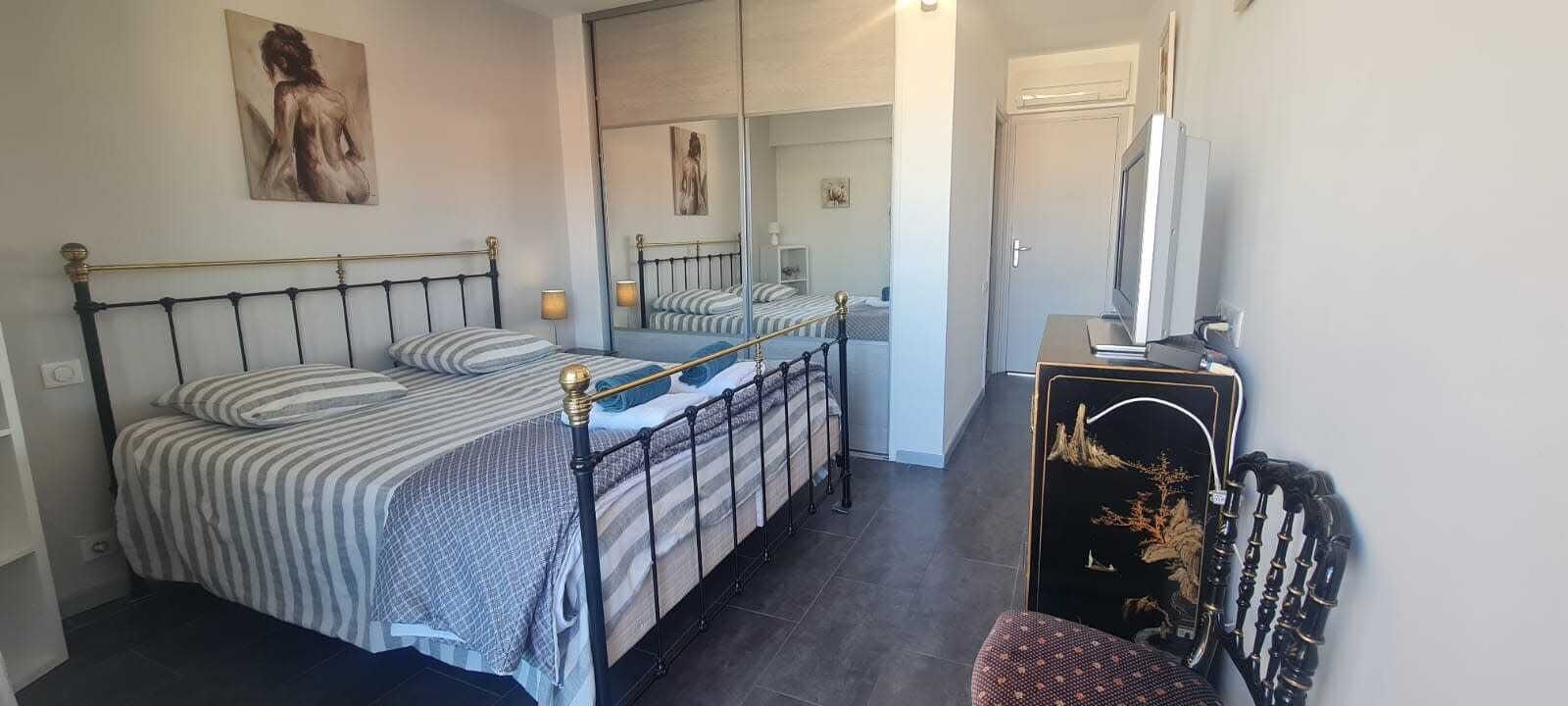 A bedroom with a bed, a mirror, a TV, and a dresser.