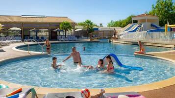 Una piscina con sillas de descanso y sombrillas, un tobogán y un edificio con tejado de tejas.