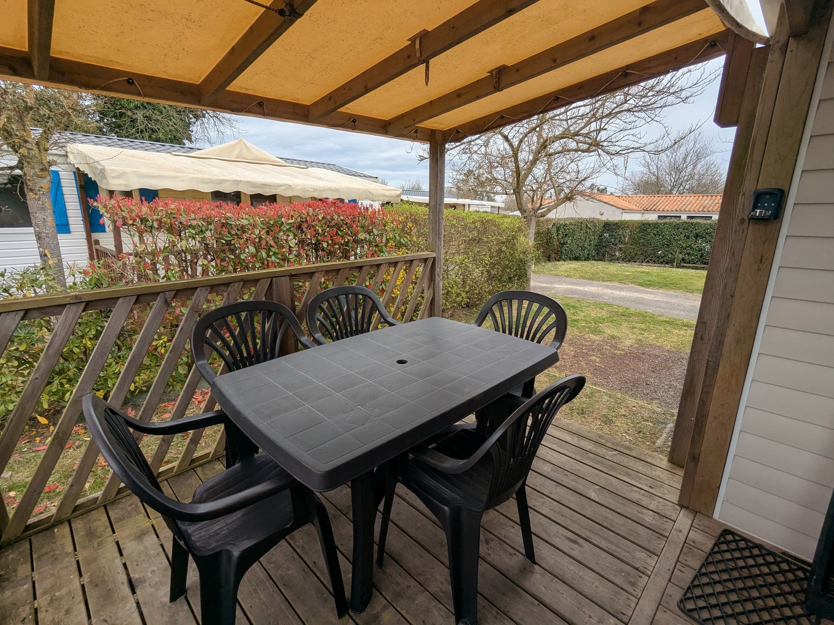 Un espacio de estar al aire libre cubierto con una mesa y sillas, una terraza de madera y vistas a una casa y jardín.