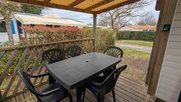 Un espacio de estar al aire libre cubierto con una mesa y sillas, una terraza de madera y vistas a una casa y jardín.