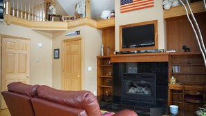 A living room with a brown leather sofa, a fireplace, a television, and a wooden staircase.