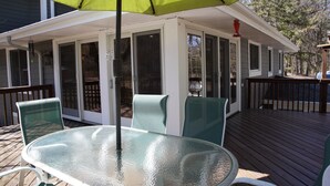A glass-top table with chairs under a green umbrella on a wooden deck.
