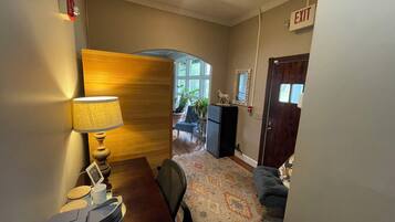 A hallway with a wooden wall, a lamp, a desk, a chair, a rug, and an exit sign.