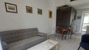 A modern living room with a grey sofa, a marble coffee table, and a dining area with a wooden table and chairs. - Central Design Flat With Parking  (Bogliasco)