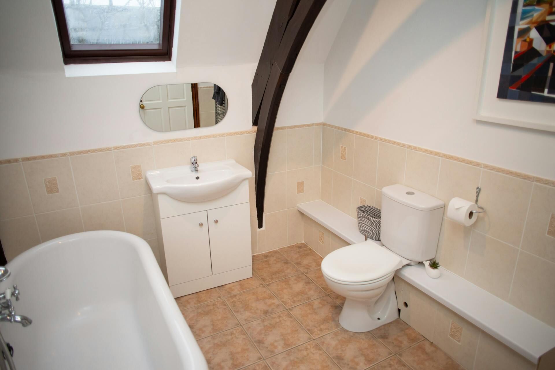 A bathroom with a bathtub, sink, toilet, and a window above the sink.
