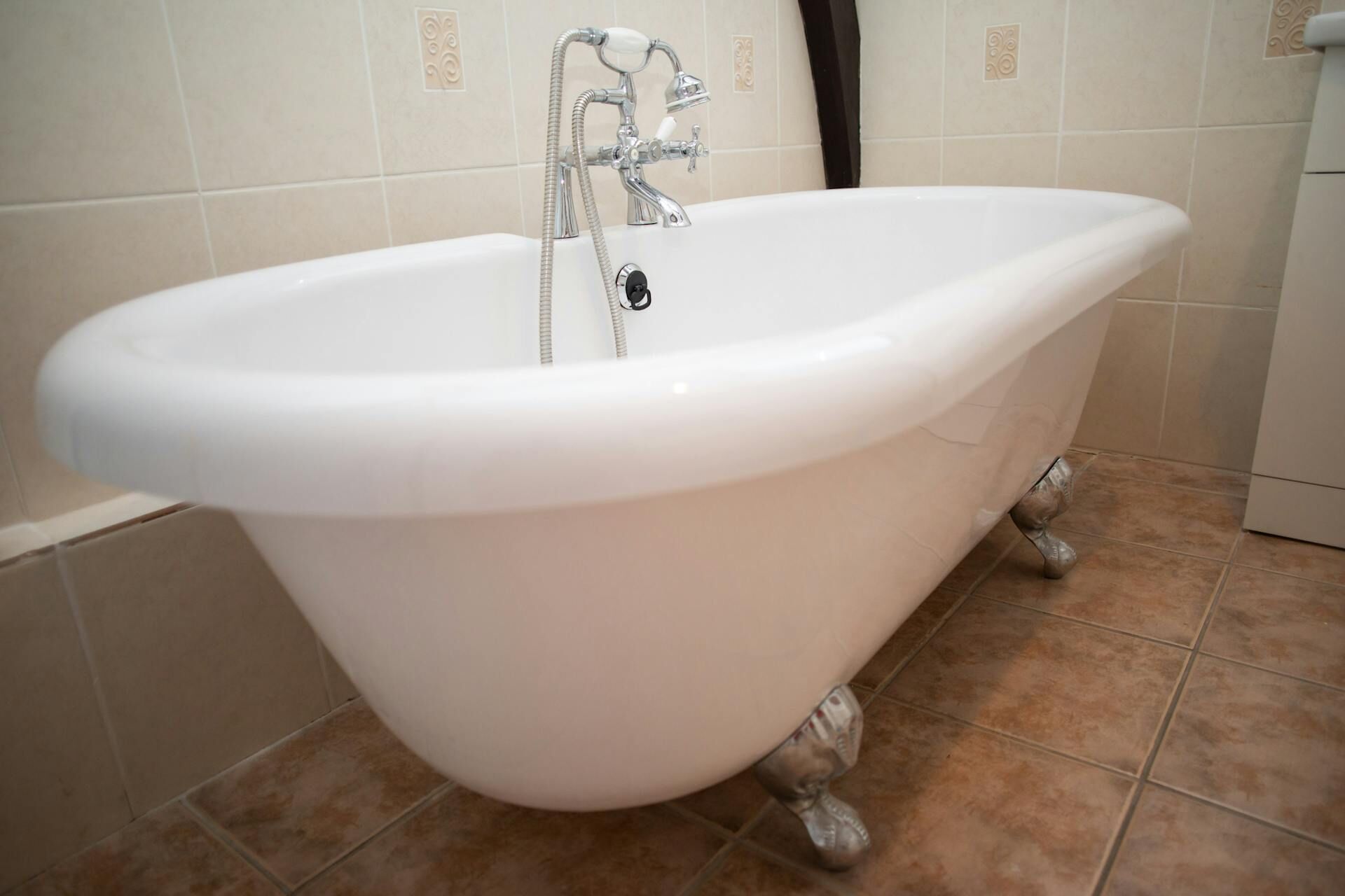A white freestanding bathtub with a single faucet and a showerhead, set against a tiled wall with decorative tiles.