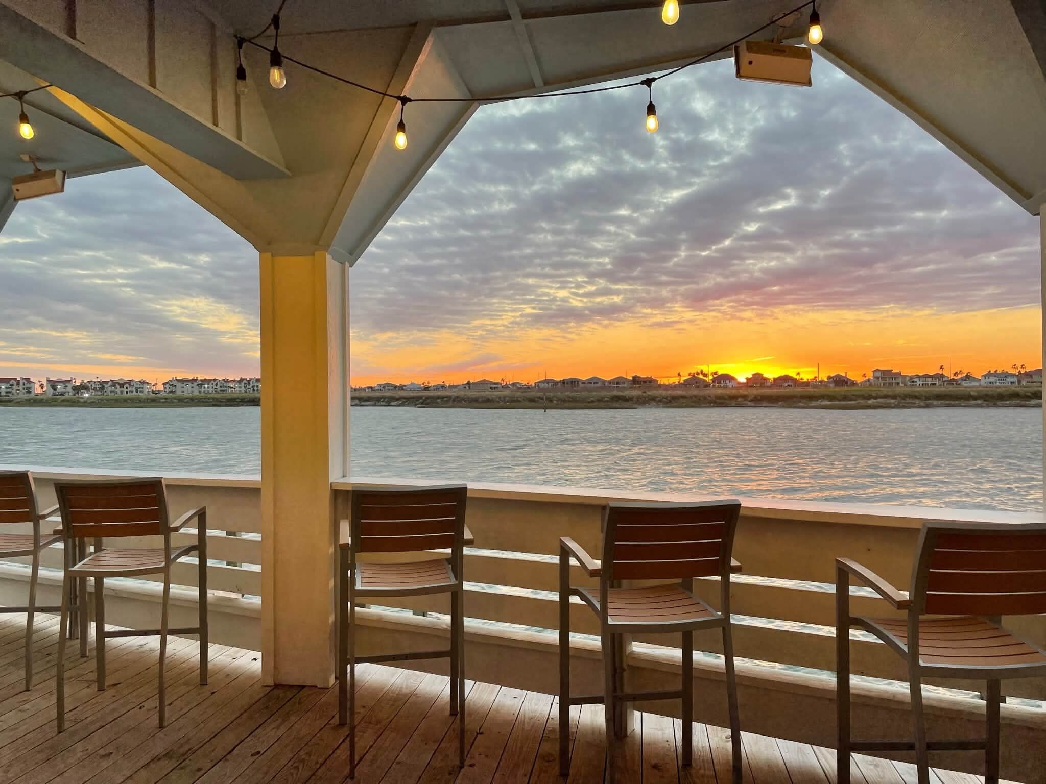 A covered outdoor seating area with chairs and a view of a sunset over water.