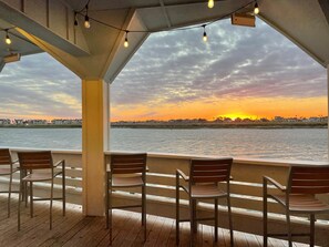 A covered outdoor seating area with chairs and a view of a sunset over water.