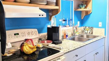 Une cuisine compacte équipée d’une cuisinière, d’un évier et de divers ustensiles de cuisine rangés sur des étagères.