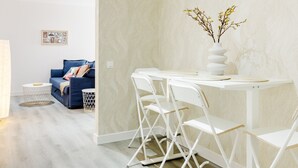 A modern dining area with a white table and chairs, a vase with flowers, and a blue sofa in the background.