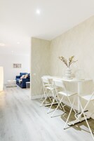 Un comedor moderno con una mesa y sillas blancas, un florero con flores y un sofá azul al fondo.