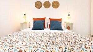 A bedroom with a floral-patterned bedspread, two blue pillows with orange accents, and two wall-mounted decorative items.