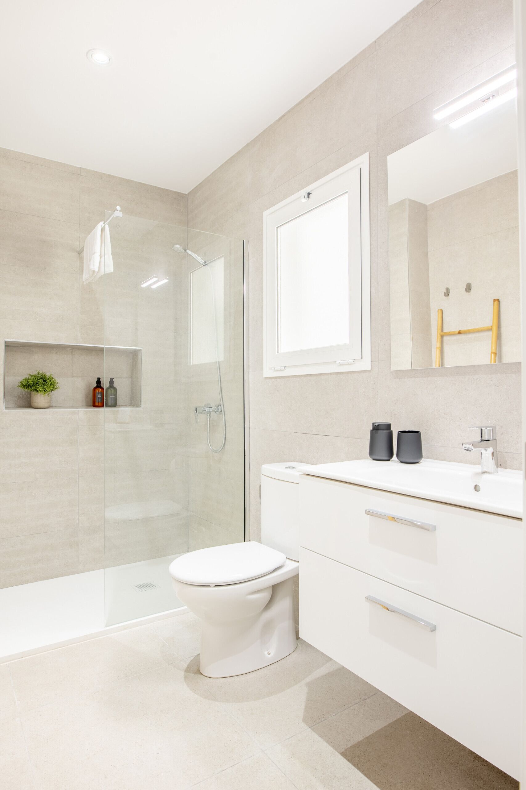 Un baño moderno con ducha envuelta en vidrio, inodoro blanco y tocador con espejo y dos recipientes negros.
