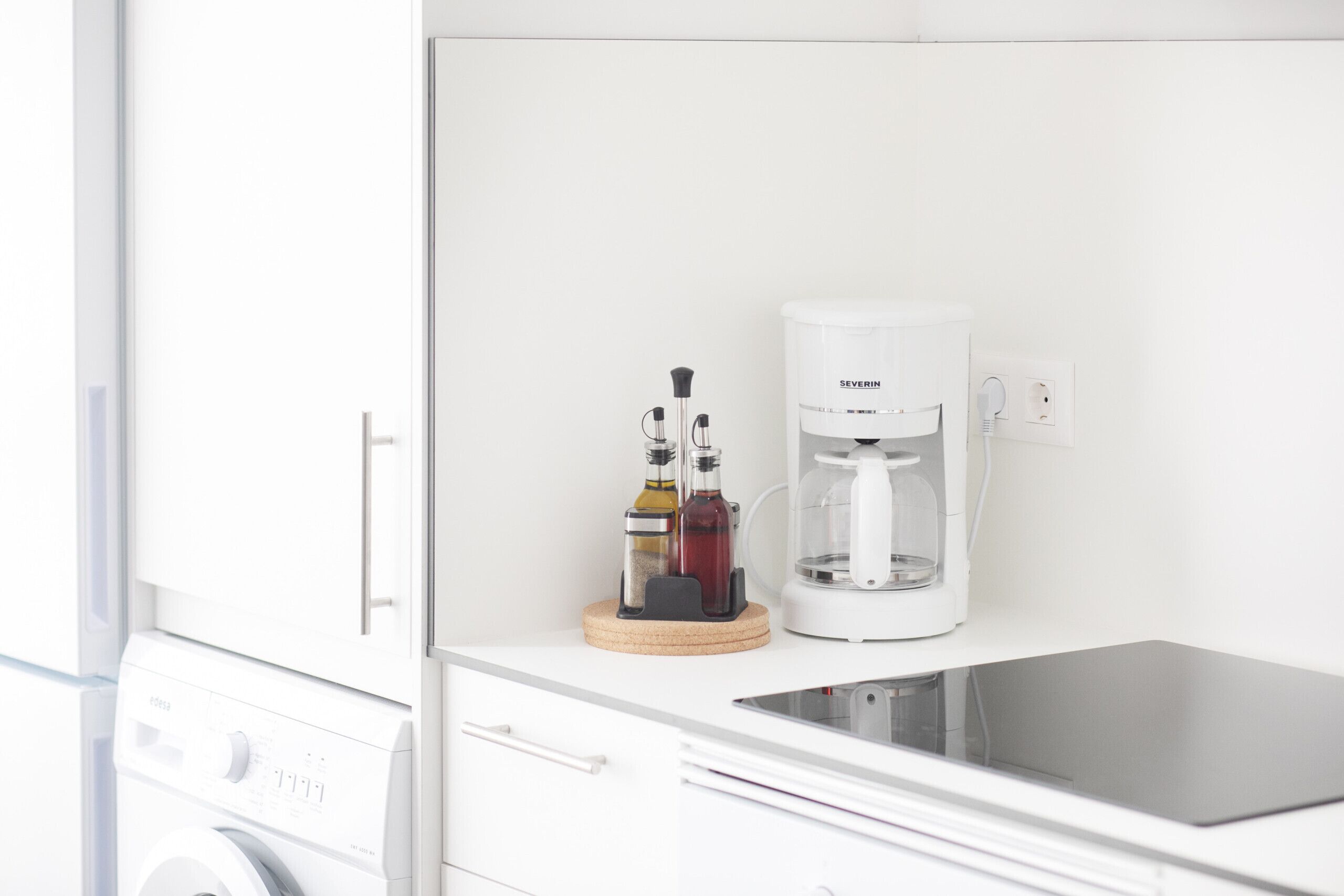 Eine moderne Küche mit Waschmaschine, Kaffeemaschine und einem Tablet auf der Arbeitsplatte.