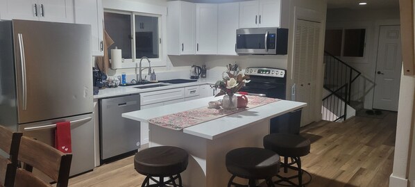 A modern kitchen with white cabinets, a stainless steel refrigerator, a microwave, and a wooden floor.