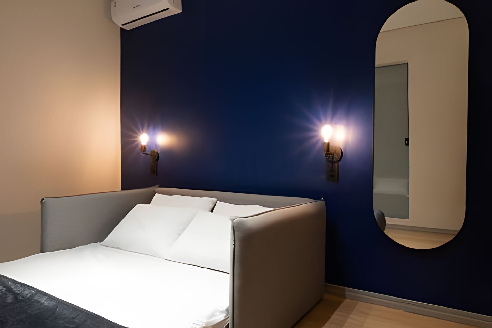 Une chambre moderne avec un lit, deux lampes fixées au mur, un grand miroir et un appareil de climatisation.