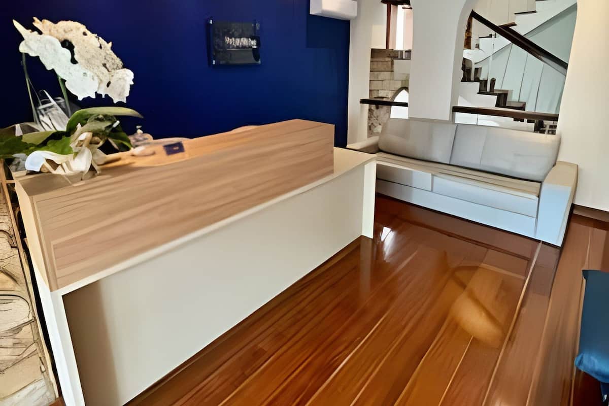 Una reception con una parete blu a contrasto, pavimento in legno e una scala con ringhiera in vetro.