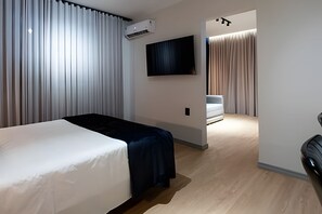 A modern hotel room with a bed, a flat-screen TV, and a seating area with a sofa and curtains. - Conde de Linhares Flats (Belo Horizonte)