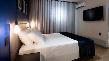 Quarto de hotel moderno com uma cama bem arrumada, uma televisão montada na parede e um aparelho de ar condicionado.