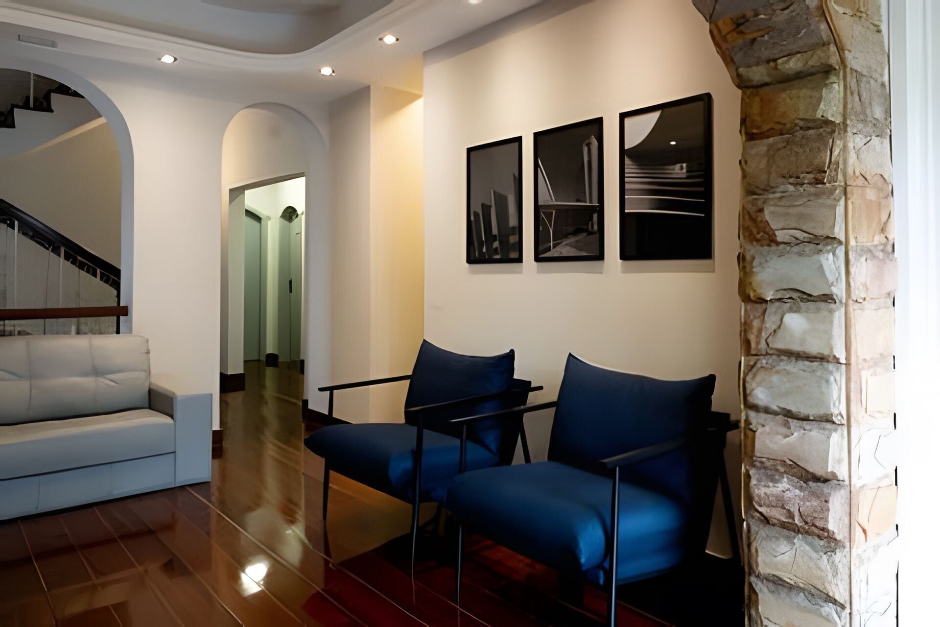 A modern living room with a white sofa, two blue armchairs, and a stone accent wall.