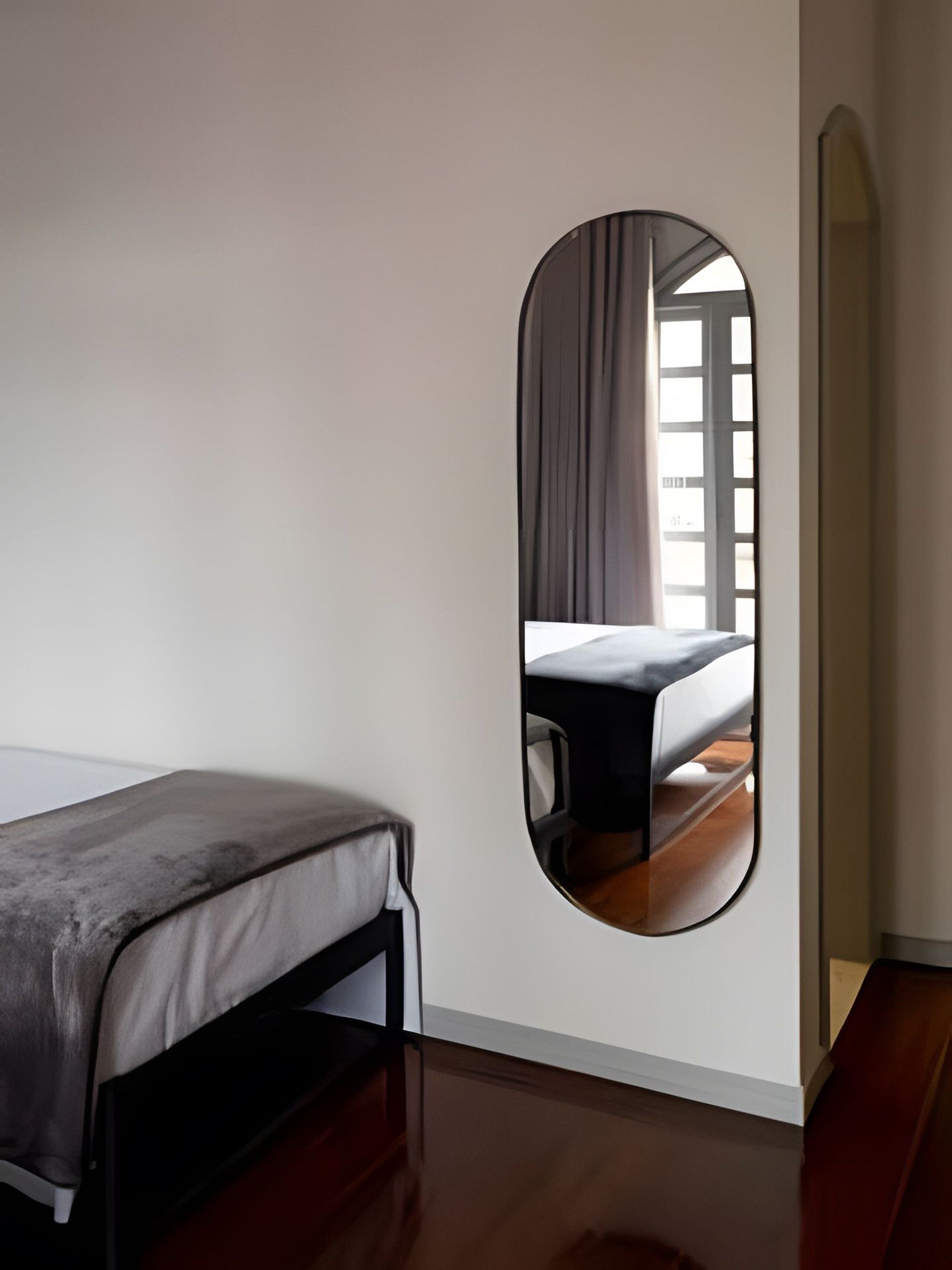 A minimalist room with a bed, a large mirror, and a window with curtains.