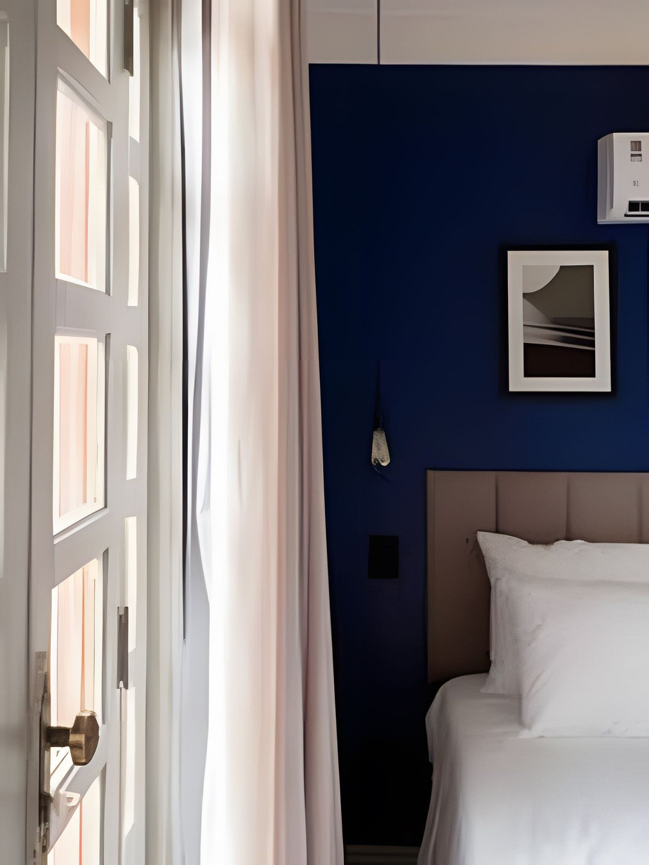 A hotel room with a bed, a wall-mounted air conditioner, and a framed picture.