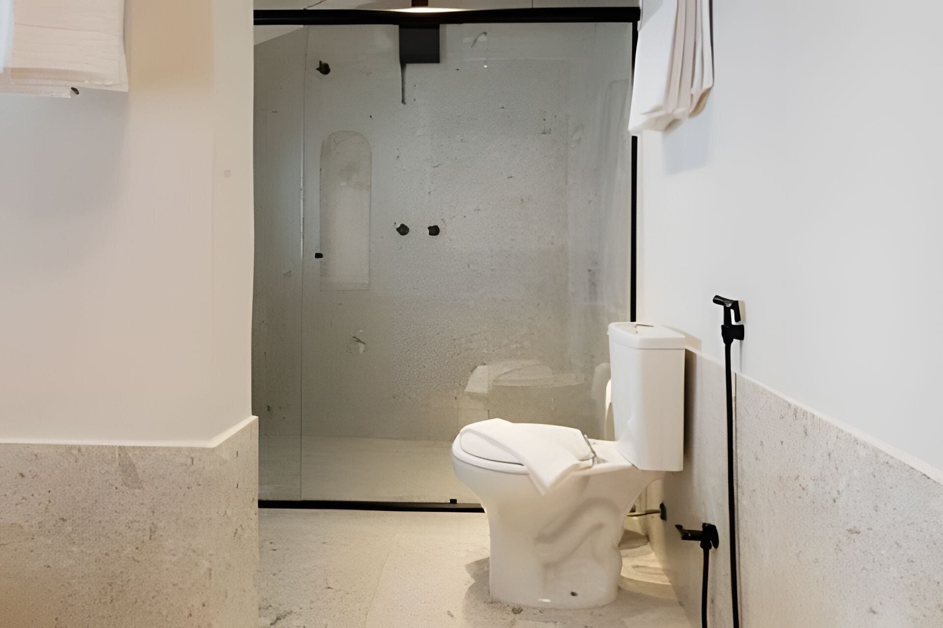 Un baño con inodoro, cabina de ducha y toalla colgada en la pared.