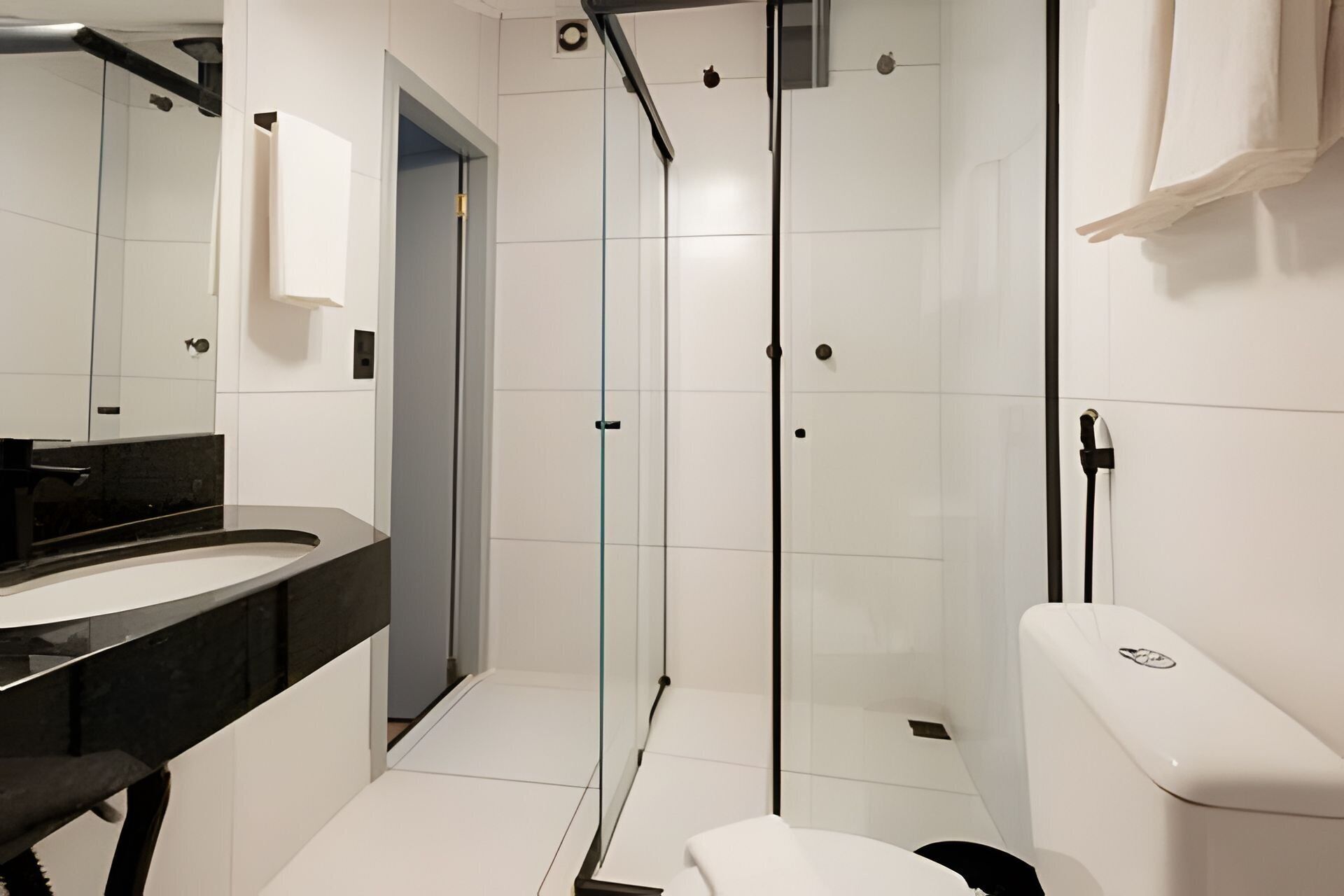A modern bathroom with a glass-enclosed shower, a black countertop sink, and a white toilet.