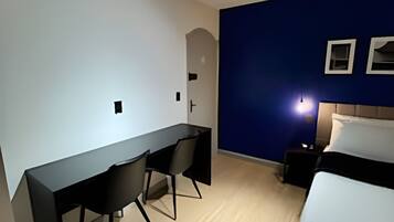 Un dormitorio con una cama, un escritorio con dos sillas, una mesita de noche y una lámpara de pared.