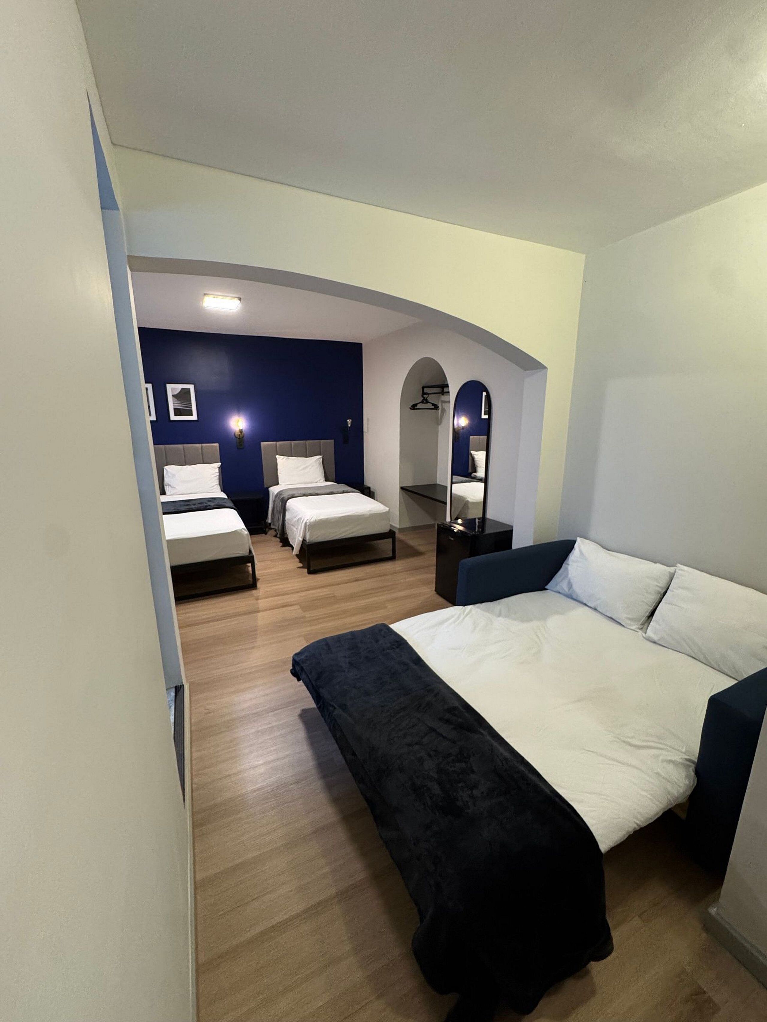 Una camera d'albergo con un letto grande, un letto più piccolo, una scrivania e uno specchio.