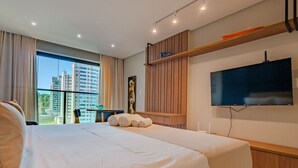 A hotel room with a large bed, a television mounted on the wall, and a view of tall buildings through the window.